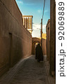 Street with adobe houses in the old city of Yazd with a view of the ventilation tower against the blue sky. 92069889