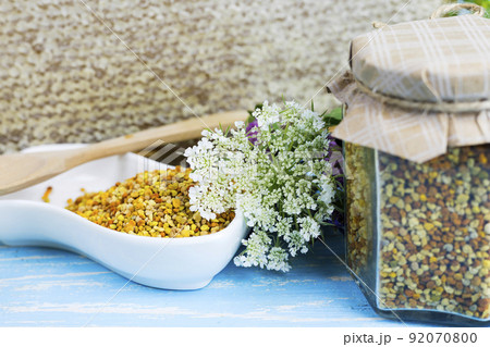 raw organic bee pollen on a wooden board surrounded by wildflowers 92070800