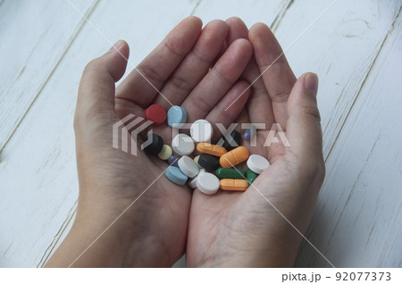 Female hand holding assorted pills isolated on wooden background. Medical concept Female hand holding assorted pills isolated on wooden background. Medical concept 92077373