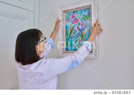 Woman hanging floral birds art framed at home on the wall Woman hanging floral birds art framed at home on the wall 92081663