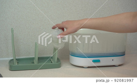 A woman removes children's dishes from a steam sterilizer and hangs them on a dryer. The sterilizer cleans germs and bacteria. 92081997