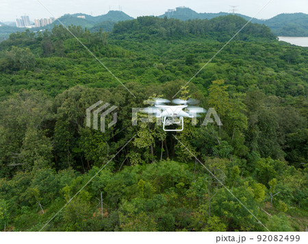 Flying white drone taking photo of landscape in forest Flying white drone taking photo of landscape in forest 92082499