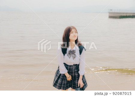 制服姿の女子高生と綺麗な海岸風景 92087015