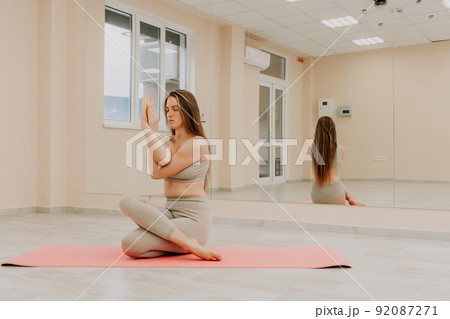 Young sporty woman, fitness instructor in sportswear doing stretching and pilates on yoga mat in the studio with mirror. Female fitness yoga routine concept. Healthy lifestyle and harmony. 92087271