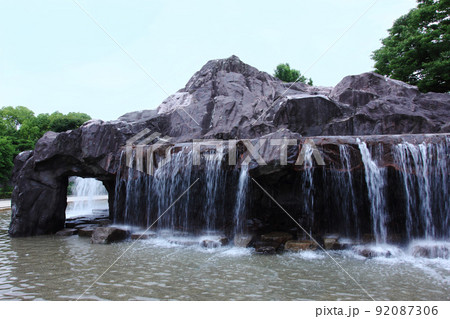 滝のある公園。岩山から落ちる水の音も激しく、公園の水遊び場は子供達を待っている 92087306