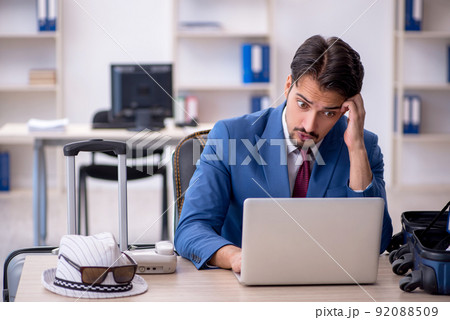 Young male employee preparing for trip at workplace Young male employee preparing for trip at workplace 92088509