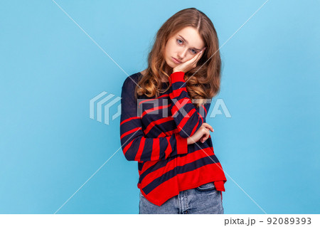Woman wearing striped casual style sweater, listening tedious story with gloomy depressed expression, being indifferent to conversation, lack of ideas. Indoor studio shot isolated on blue background. Woman wearing striped casual style sweater, listening tedious story with gloomy depressed expression, being indifferent to conversation, lack of ideas. Indoor studio shot isolated on blue background. 92089393