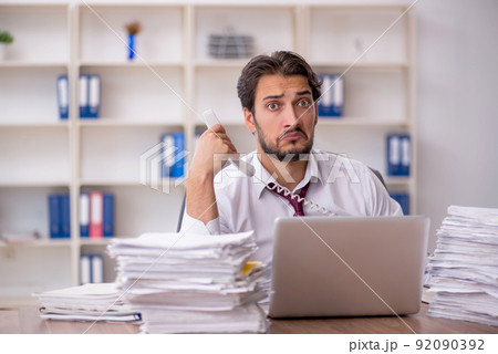 Young male employee and too much work in the office Young male employee and too much work in the office 92090392