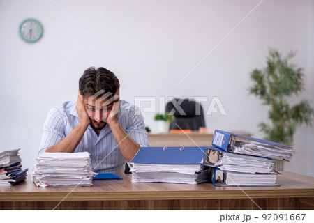 Young male employee and too much work in the office Young male employee and too much work in the office 92091667