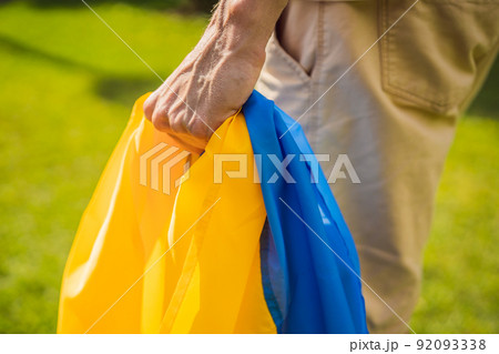 A man holds a Ukrainian flag in his hands. concept Ukrainian patriot, rally in support of Ukraine A man holds a Ukrainian flag in his hands. concept Ukrainian patriot, rally in support of Ukraine 92093338