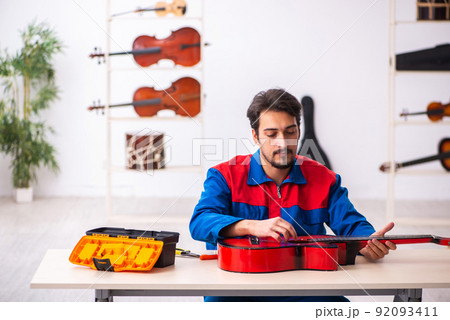 Young male repairman repairing musical instruments at workplace Young male repairman repairing musical instruments at workplace 92093411