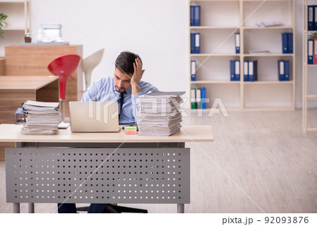 Young male employee and too much work in the office Young male employee and too much work in the office 92093876