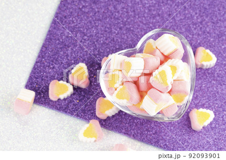 Colorful miniature marshmallows in a love shape glass on a purple white background Colorful miniature marshmallows in a love shape glass on a purple white background 92093901