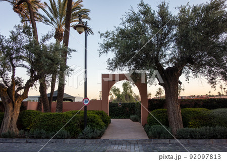 モロッコの街マラケシュウノ街並み　ヤシの木と緑に囲まれた赤茶色の壁の門 92097813