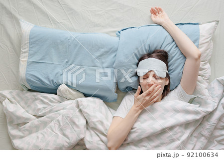 woman lies in bed and yawns or sleeps with a sleeping mask on her face. a European woman with sleep problems and insomnia 92100634