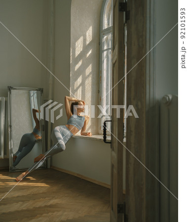 Fitness, yoga, stretching and healthy lifestyle concept - young woman doing exercises near window at home Fitness, yoga, stretching and healthy lifestyle concept - young woman doing exercises near window at home 92101593