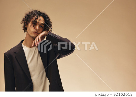 Defiant awesome tanned curly man in classic brown jacket touches curls posing isolated on over beige pastel background. Fashion New Collection offer. Retro style concept. Free place for ad Defiant awesome tanned curly man in classic brown jacket touches curls posing isolated on over beige pastel background. Fashion New Collection offer. Retro style concept. Free place for ad 92102015