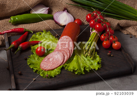 smoked servelat on a wooden board decorated with fresh vegetables smoked servelat on a wooden board decorated with fresh vegetables 92103039