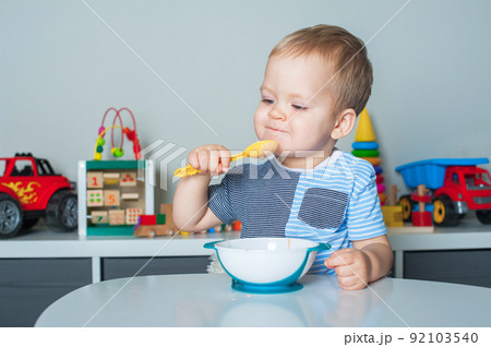 Toddler boy eats with spoon and is covered in food. Baby food, food allergies, self-feeding.... Toddler boy eats with spoon and is covered in food. Baby food, food allergies, self-feeding.... 92103540