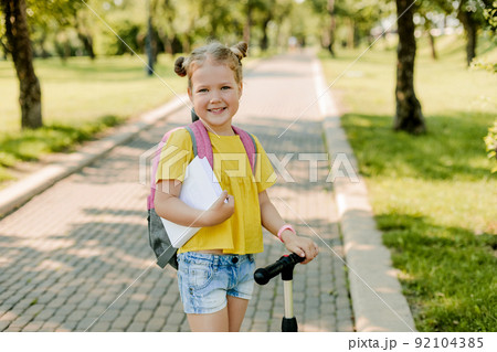 A beautiful little girl rides a scooter on her way back to school 92104385