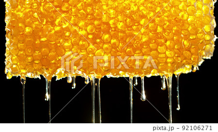 Honey dripping from honey comb on black background. 92106271