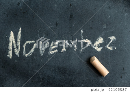 November. Name of autumn month written in yellow chalk on black chalk board. Handwritten text. A piece of colored chalk lies next to it. November. Name of autumn month written in yellow chalk on black chalk board. Handwritten text. A piece of colored chalk lies next to it. 92106387