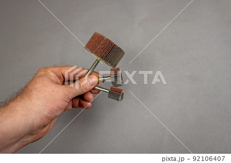 A man's hand holds the Grinding Blade Wheels. A tool for woodworking as well as stripping surfaces of corrosion, scale or rust. Side view. Gray background. Selective focus. A man's hand holds the Grinding Blade Wheels. A tool for woodworking as well as stripping surfaces of corrosion, scale or rust. Side view. Gray background. Selective focus. 92106407