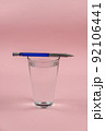 A glass of water and a pencil on a pink background. A full glass of drinking water. Blue and silver metallic pencil. Kurp plan. Selective focus. 92106441