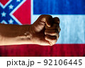 Tightly clenched male fist in front of state Mississippi flag. Concept of independence, freedom, and unity. Selective focus. 92106445