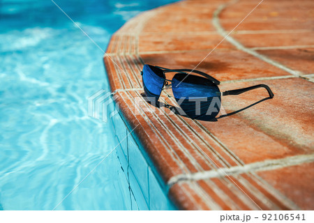 Sunglasses on side of pool with clear turquoise water. No people copy space Sunglasses on side of pool with clear turquoise water. No people copy space 92106541