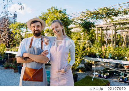 Owners of garden centre in aprons are looking to camera. Copyspace 92107040