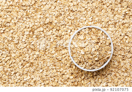 ceramic plate with dry rolled oats on a oat flakes background close-up top view. 92107075