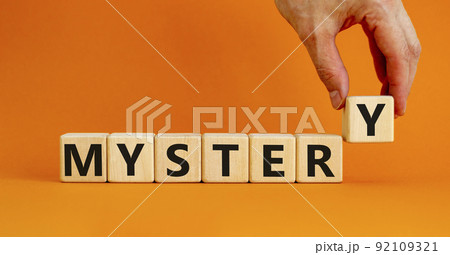Mystery symbol. The concept word Mystery on wooden cubes. Beautiful orange table, orange background, copy space. Businessman hand. Business and mystery mysterious concept. 92109321