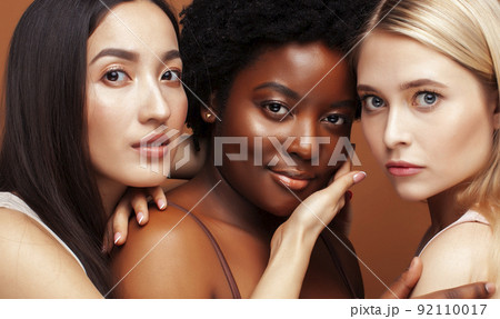 young pretty african and caucasian women posing cheerful together on brown background, lifestyle diverse nationality people concept close up young pretty african and caucasian women posing cheerful together on brown background, lifestyle diverse nationality people concept close up 92110017