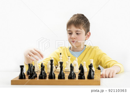 Serious schoolboy plays chess. Portrait of child during chess game. Isolated on white background. Serious schoolboy plays chess. Portrait of child during chess game. Isolated on white background. 92110363