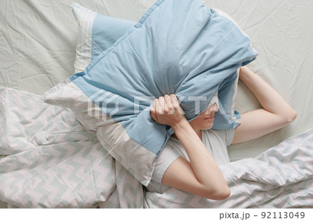 woman lies in bed and covers her head with pillows. the woman suffers from insomnia or sleep disorders 92113049