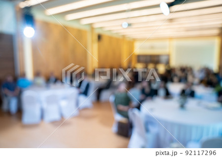 Blurry seminar hall with audience student in it. This room are arranged by round circle group table that appropriate for workshop. 92117296
