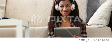 Latin young woman sit on carpet with tablet and watch show, lady in headset Latin young woman sit on carpet with tablet and watch show, lady in headset 92124828