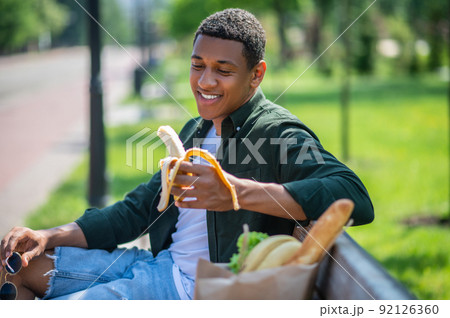 Guy looking at banana sitting on bench Guy looking at banana sitting on bench 92126360