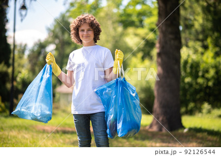 Young volunteer with bags full of [plastic garbage Young volunteer with bags full of [plastic garbage 92126544