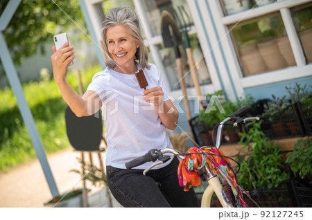 Cheerful woman on a bike eating ice-cream and looking happy Cheerful woman on a bike eating ice-cream and looking happy 92127245