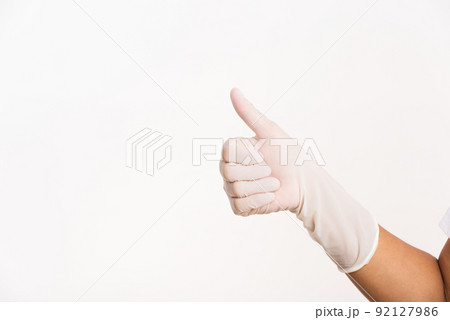 Woman wearing hand to blue rubber medical glove with thumb up finger 92127986