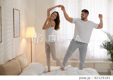 Lovely young couple dancing on bed at home Lovely young couple dancing on bed at home 92129185
