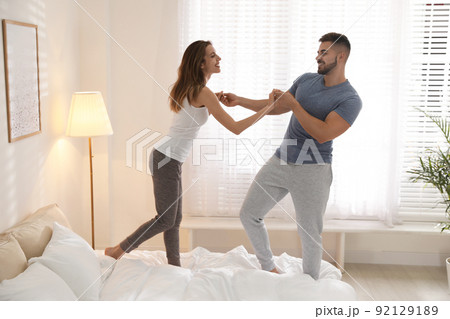 Lovely young couple dancing on bed at home Lovely young couple dancing on bed at home 92129189