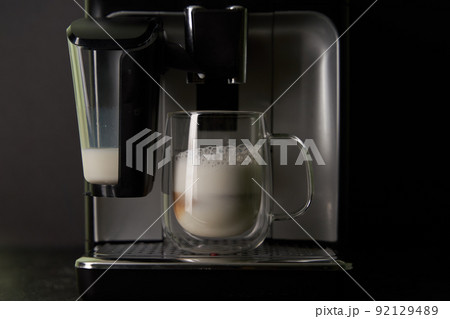 Freshly brewed cappuccino is poured from the coffee machine into glass cups. Freshly brewed cappuccino is poured from the coffee machine into glass cups. 92129489