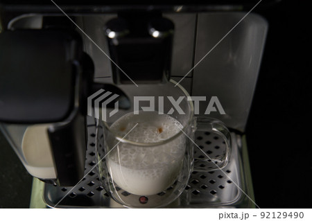 Freshly brewed cappuccino is poured from the coffee machine into glass cups. 92129490