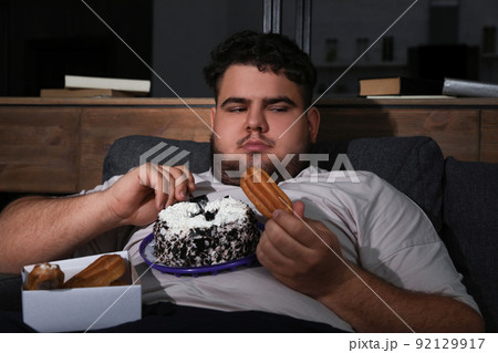 Depressed overweight man eating sweets in living room at night 92129917