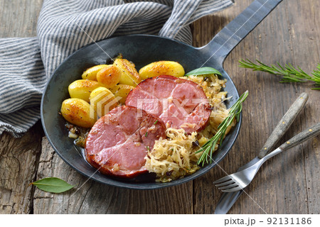 Smoked neck of pork with sauerkraut and fried baby potatoes served in an iron frying pan Smoked neck of pork with sauerkraut and fried baby potatoes served in an iron frying pan 92131186