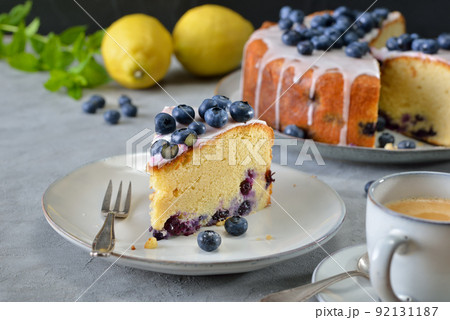 Lemon blueberry cake covered with sweet sugar icing and berries, served with coffee Lemon blueberry cake covered with sweet sugar icing and berries, served with coffee 92131187