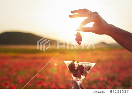 Strawberries in a glass against a field of poppies in the setting sun. Front view. 92131537